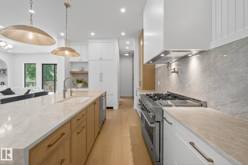 Gourmet kitchen featuring a large central island with integrated sink, stainless steel appliances including a range with griddle, wood-finish flooring, and pendant lighting - 13804 85 Avenue, Edmonton, AB - Indoor Photo Showing Kitchen With Upgraded Kitchen