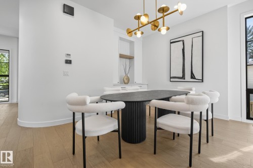 Dining area with light wood-finish flooring, a contemporary gold-toned chandelier, and a built-in display niche with a wood shelf - 13804 85 Avenue, Edmonton, AB - Indoor Photo Showing Dining Room
