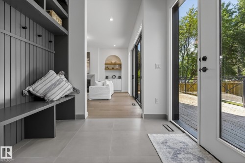 Foyer featuring large format tile flooring, built-in bench with beadboard detailing, integrated shelving, and a full-light entry door leading to an exterior deck - 13804 85 Avenue, Edmonton, AB - Indoor Photo Showing Other Room