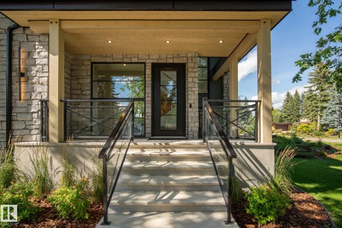 Stone facade entry with a full-light door, covered porch, wood-finish ceiling with recessed lighting, and glass panel railings - 13804 85 Avenue, Edmonton, AB - Outdoor With Deck Patio Veranda