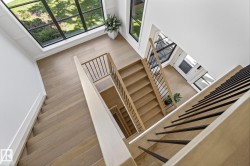 Multi-level interior staircase featuring light wood-finish treads and risers, contemporary black metal balusters, and a solid wood handrail - 