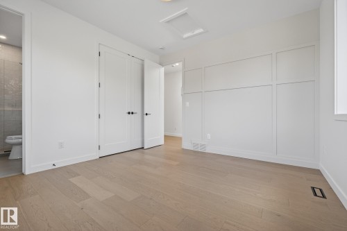 Spacious room featuring light wood-finish flooring, white panel-style doors with matte black hardware, and a decorative wainscoting wall accent - 13804 85 Avenue, Edmonton, AB - Indoor Photo Showing Other Room
