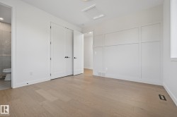 Spacious room featuring light wood-finish flooring, white panel-style doors with matte black hardware, and a decorative wainscoting wall accent - 
