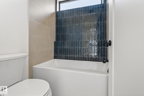 Bathroom featuring a white soaking tub with matte black fixtures, an accent wall of dark blue vertical subway tile, and light beige wall tiles - 13804 85 Avenue, Edmonton, AB - Indoor Photo Showing Bathroom