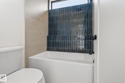 Bathroom featuring a white soaking tub with matte black fixtures, an accent wall of dark blue vertical subway tile, and light beige wall tiles - 