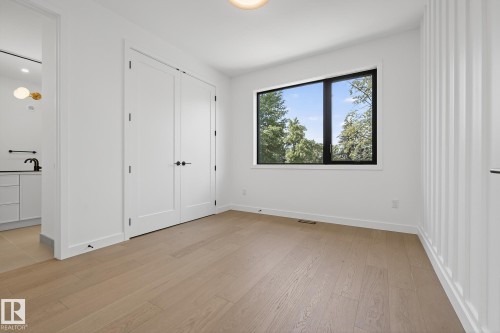 Open concept room featuring wood-finish flooring, a large black-framed window, and white double closet doors - 13804 85 Avenue, Edmonton, AB - Indoor Photo Showing Other Room
