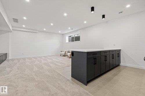 Spacious room featuring a dark gray cabinet island with a light-toned countertop, recessed ceiling lighting, a window, and mixed flooring of patterned carpet and large format tiles - 13804 85 Avenue, Edmonton, AB - Indoor
