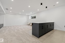 Spacious room featuring a dark gray cabinet island with a light-toned countertop, recessed ceiling lighting, a window, and mixed flooring of patterned carpet and large format tiles - 