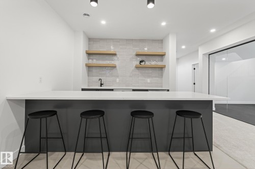 Contemporary wet bar featuring a solid surface countertop, matte black faucet, and light wood-finish floating shelves on a tiled backsplash - 13804 85 Avenue, Edmonton, AB - Indoor