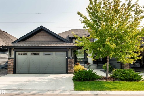 Contemporary single-story residence featuring a two-car garage with a light grey door, stacked stone accents, and a dark shingled roof - 3 8050 Orchards Green, Edmonton, AB 