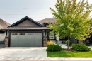 Contemporary single-story residence featuring a two-car garage with a light grey door, stacked stone accents, and a dark shingled roof - 3 8050 Orchards Green, Edmonton, AB 