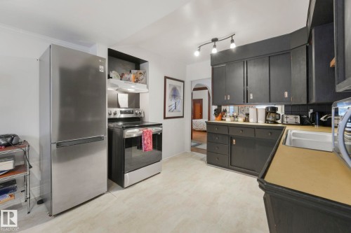 Kitchen featuring a stainless steel refrigerator, stainless steel electric range with overhead vent, dark cabinetry, and light-toned flooring - 5043 48 St Nw, Sylvan Lake, AB - Indoor Photo Showing Kitchen