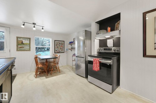 Kitchen featuring stainless steel appliances, a built-in range hood with upper cabinetry, and light-tone flooring - 5043 48 St Nw, Sylvan Lake, AB - Indoor Photo Showing Kitchen