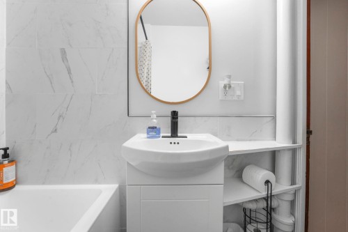 Bathroom featuring white subway tile with subtle grey veining, a white vanity with integrated sink, matte black faucet, and an oval gold-framed mirror - 5043 48 St Nw, Sylvan Lake, AB - Indoor Photo Showing Bathroom