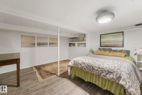 Spacious room featuring wood-finish flooring, white paneled wall accents, built-in shelving, and a modern flush-mount ceiling light - 5043 48 St Nw, Sylvan Lake, AB - Indoor Photo Showing Bedroom