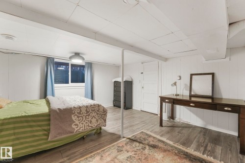 Finished room featuring wood-finish flooring, white paneling, and a window with privacy blinds - 5043 48 St Nw, Sylvan Lake, AB - Indoor Photo Showing Bedroom