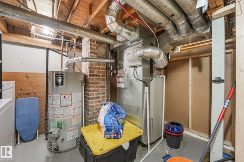 Mechanical room featuring a water heater, furnace, exposed brick, and utility lighting - 5043 48 St Nw, Sylvan Lake, AB - Indoor Photo Showing Basement