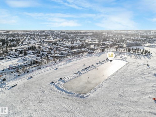 Expansive snow-covered landscape with a cleared ice surface featuring recreational activity, bordered by a tree-lined street and residential buildings - 5043 48 St Nw, Sylvan Lake, AB - Outdoor With View