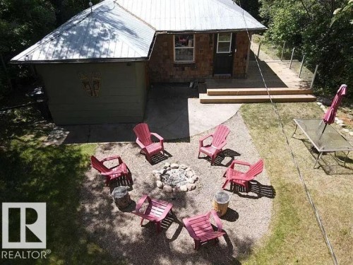 Backyard living space featuring a gravel fire pit area, concrete patio, and sloped grassed sections - 5043 48 St Nw, Sylvan Lake, AB - Outdoor