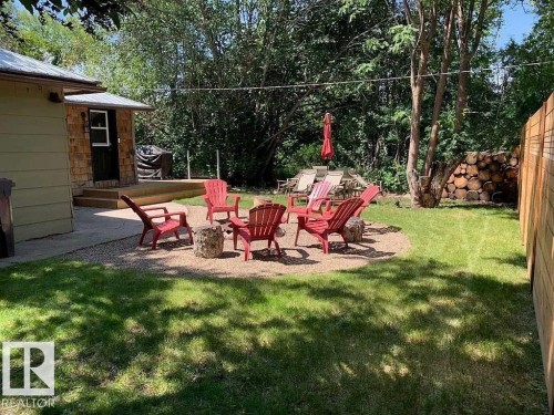 Expansive backyard featuring a stone fire pit area, manicured lawn, wood privacy fencing, and mature trees - 5043 48 St Nw, Sylvan Lake, AB - Outdoor