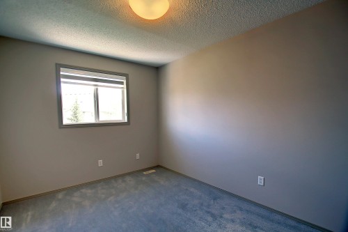Neutral-toned room featuring a single window with a white frame, textured ceiling, and blue carpet flooring - 8129 7 Avenue, Edmonton, AB - Indoor Photo Showing Other Room