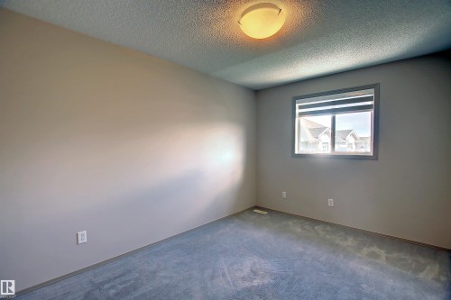 Neutral tone walls with gray trim, light blue-gray carpeting, and a flush mount ceiling light fixture - 8129 7 Avenue, Edmonton, AB - Indoor Photo Showing Other Room
