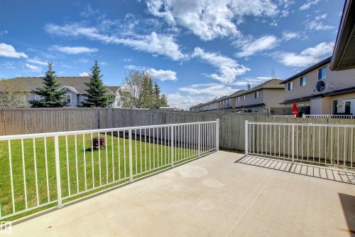 Expansive concrete patio with white metal railings and gate, overlooking a fenced backyard with green lawn - 8129 7 Avenue, Edmonton, AB - Outdoor