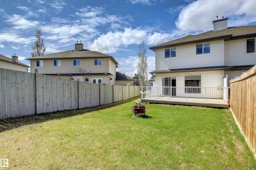 Expansive fenced backyard featuring a wooden deck with white railings, a sliding glass door, a fire pit, and a manicured lawn - 8129 7 Avenue, Edmonton, AB - Outdoor With Deck Patio Veranda With Exterior