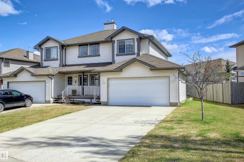 Two-story duplex featuring white siding, dark trim, and a prominent two-car garage - 8129 7 Avenue, Edmonton, AB - Outdoor With Facade
