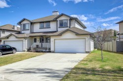 Two-story duplex featuring white siding, dark trim, and a prominent two-car garage - 