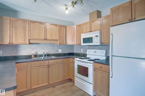 Kitchen featuring natural wood-finish cabinetry, a double basin stainless steel sink, and a tiled backsplash - 8129 7 Avenue, Edmonton, AB - Indoor Photo Showing Kitchen With Double Sink