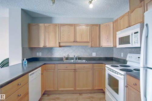 Kitchen featuring wood-finish cabinetry, dark countertops, and a tiled backsplash - 8129 7 Avenue, Edmonton, AB - Indoor Photo Showing Kitchen With Double Sink