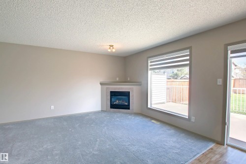 Living area featuring light gray walls, textured ceiling, and soft blue carpeting - 8129 7 Avenue, Edmonton, AB - Indoor Photo Showing Living Room With Fireplace