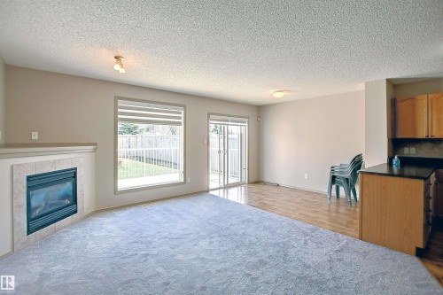 Living area featuring a gas fireplace with a tiled surround, a large window overlooking the fenced backyard, and a sliding glass door providing exterior access - 8129 7 Avenue, Edmonton, AB - Indoor Photo Showing Living Room With Fireplace