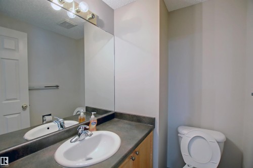Bathroom vanity with an integrated sink, a dark countertop, and wood-finish cabinetry - 8129 7 Avenue, Edmonton, AB - Indoor Photo Showing Bathroom