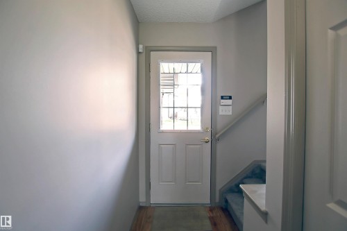 Entryway featuring a paneled door with an upper window insert, wood-finish flooring, and a carpeted staircase with a handrail - 8129 7 Avenue, Edmonton, AB - Indoor Photo Showing Other Room