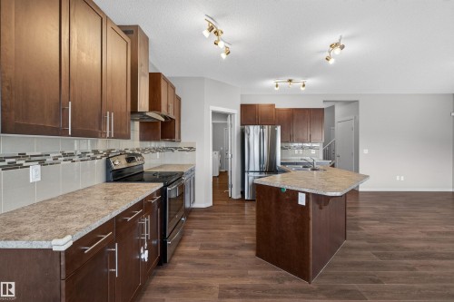 Kitchen featuring wood-finish cabinetry, stainless steel appliances, a center island with a composite countertop, and coordinated backsplash tiling - 4723 Alwood Bend Sw, Edmonton, AB - Indoor Photo Showing Kitchen With Stainless Steel Kitchen With Upgraded Kitchen