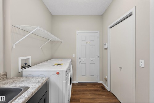Laundry area featuring wood-finish flooring, a utility sink with a laminate countertop, and overhead wire shelving - 4723 Alwood Bend Sw, Edmonton, AB - Indoor Photo Showing Laundry Room