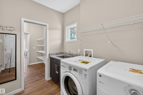 Functional utility area featuring wood-finish flooring, a built-in sink with a granite-style countertop, dark wood cabinetry, and a window providing natural light - 4723 Alwood Bend Sw, Edmonton, AB - Indoor Photo Showing Laundry Room