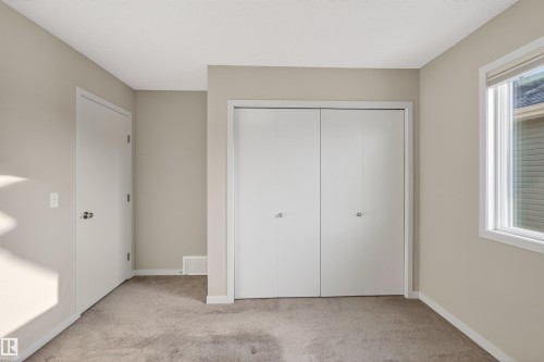 Neutral-toned room featuring a window with a white frame, bi-fold closet doors, a white interior door, and plush carpeting - 4723 Alwood Bend Sw, Edmonton, AB - Indoor Photo Showing Other Room