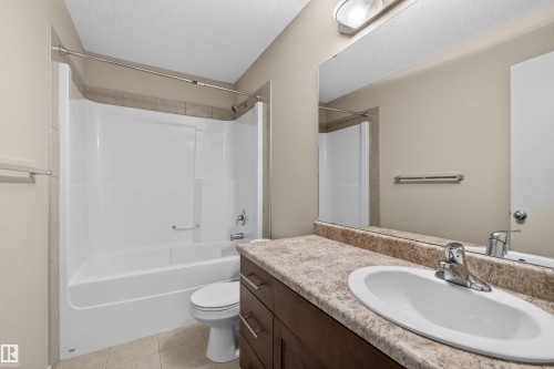 Bathroom featuring an integrated bathtub and shower, a single vanity with an undermount sink, a stone-look countertop, dark wood-finish cabinetry, and tiled flooring - 4723 Alwood Bend Sw, Edmonton, AB - Indoor Photo Showing Bathroom