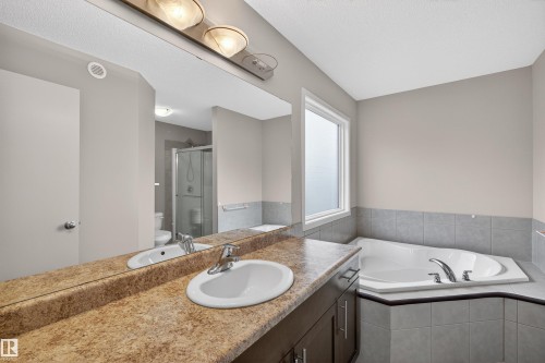 Bathroom featuring an integrated vanity with a single basin sink, an expansive wall mirror, an adjacent window-lit corner soaking tub, and a separate glass-enclosed shower - 4723 Alwood Bend Sw, Edmonton, AB - Indoor Photo Showing Bathroom