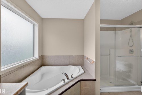 Soaking tub with chrome fixtures, tiled surround, and frosted window - 4723 Alwood Bend Sw, Edmonton, AB - Indoor Photo Showing Bathroom