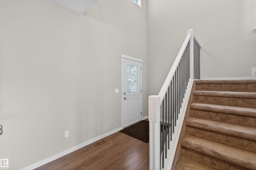 Entryway featuring wood-finish flooring, a white paneled door with decorative glass, and a carpeted staircase with white newel posts and dark balusters - 4723 Alwood Bend Sw, Edmonton, AB - Indoor Photo Showing Other Room