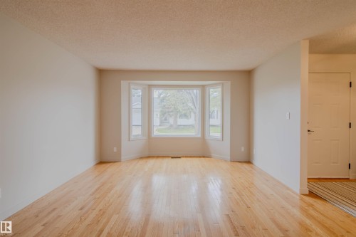 Hardwood flooring complements neutral wall tones in this spacious room featuring a prominent bay window - 5935 189 Street, Edmonton, AB - Indoor Photo Showing Other Room