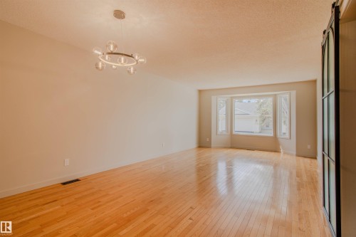 Spacious room featuring wood flooring, a contemporary chandelier, a large bay window, and light-toned walls - 5935 189 Street, Edmonton, AB - Indoor Photo Showing Other Room