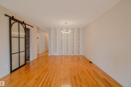 Open-concept room featuring wood flooring, a decorative accent wall, and a contemporary chandelier - 5935 189 Street, Edmonton, AB - Indoor Photo Showing Other Room