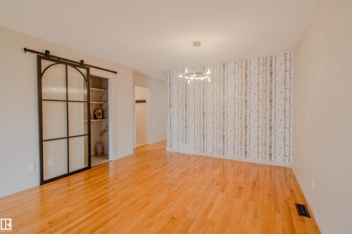 Hardwood flooring throughout, featuring a distinctive accent wall, contemporary ceiling light fixture, and a black-framed barn door revealing built-in shelving - 5935 189 Street, Edmonton, AB - Indoor Photo Showing Other Room