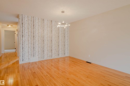 Hardwood flooring extends throughout this space, featuring a distinct accent wall with a tree-patterned design - 5935 189 Street, Edmonton, AB - Indoor Photo Showing Other Room