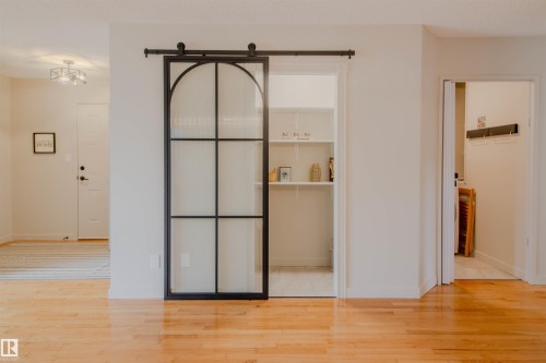 Hardwood-finish flooring extending through an interior space featuring a black-framed barn door with frosted glass panels - 5935 189 Street, Edmonton, AB - Indoor Photo Showing Other Room
